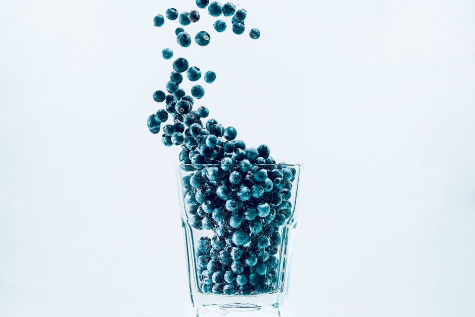 Fresh dark blue blueberries scattered on a clean white background with some berries in a clear glass bowl